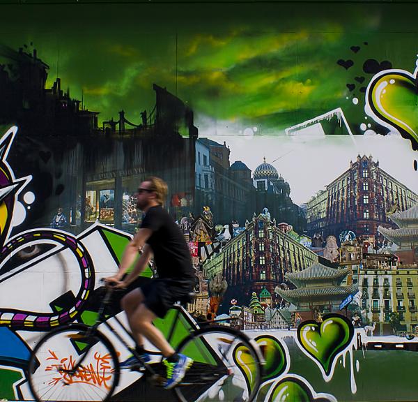 A cyclist rides past a graffiti wall covered with green hearts