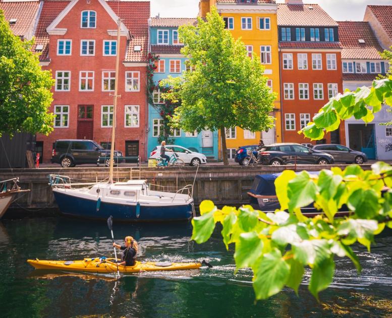 Woman kayaking past coloured houses in Christianshavn